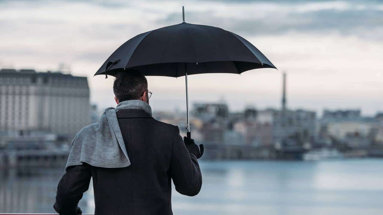 Homem segurando guarda-chuva olhando para paisagem em ponte