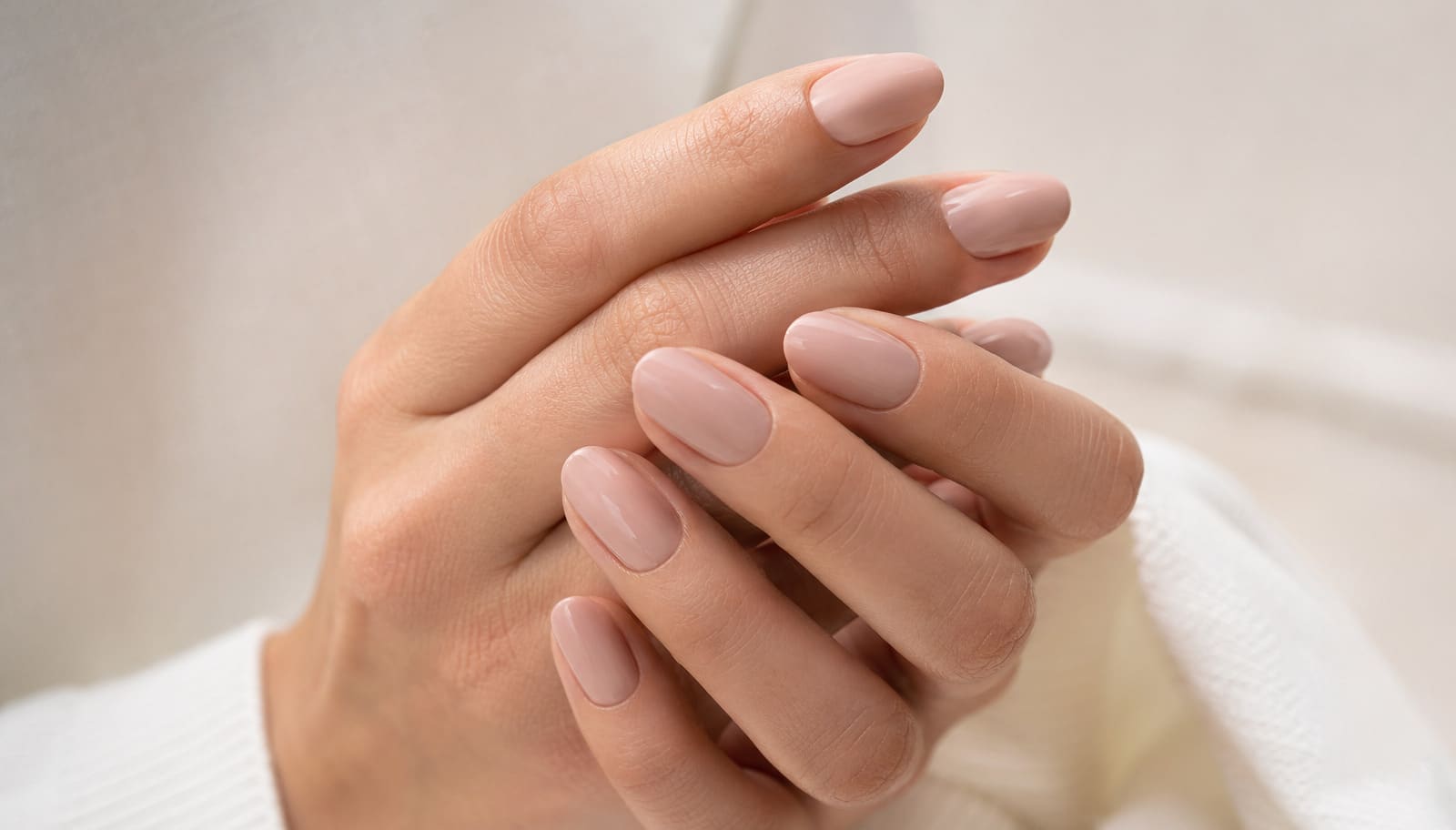 Mãos femininas exibindo unhas com esmalte rosa quartzo