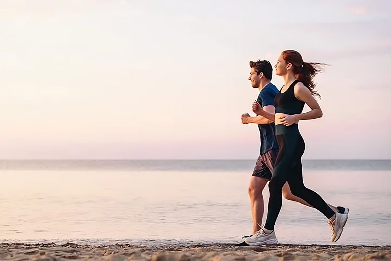 A fit couple running on the beach, staying active to support both physical health and cognitive function.