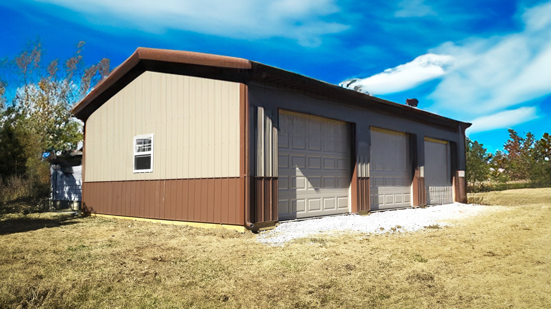 The image shows a rectangular post-frame building with a dual-tone exterior: light beige upper walls and dark brown lower siding and roof. It features three large garage doors, indicating its use as a workshop or storage facility. A small window is presen