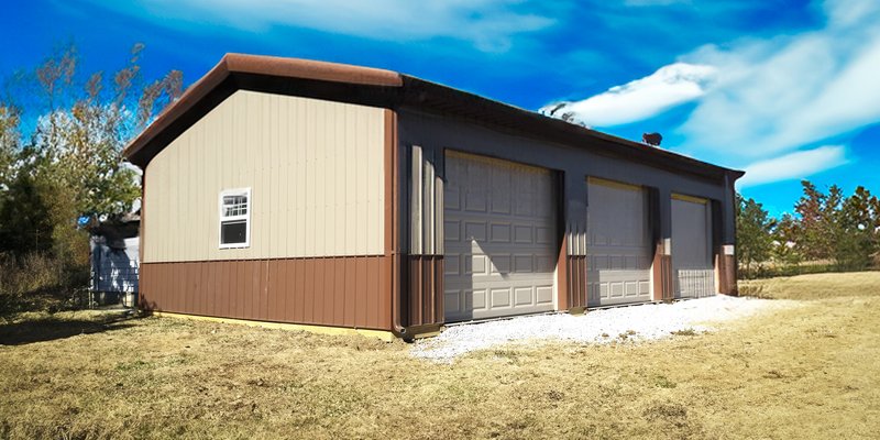 The image shows a rectangular post-frame building with a dual-tone exterior: light beige upper walls and dark brown lower siding and roof. It features three large garage doors, indicating its use as a workshop or storage facility. A small window is presen