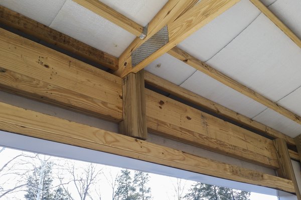 The image showcases a post-frame construction by Built-Mor Buildings, highlighting key structural elements such as wooden beams, posts, and trusses. The ceiling is insulated with a visible layer of white material, while metal fasteners secure the connecti