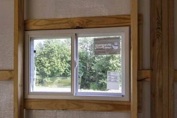 The image features a post-frame construction window from Built-Mor Buildings. The window is set in a wooden frame, suggesting sturdy support, with visible insulation wrapping the surrounding structure. The window is a sliding type and has labels indicatin