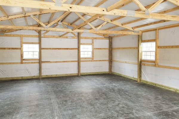 Interior of a post-frame building by Built-Mor Buildings, featuring exposed wooden trusses and beams supporting a pitched roof. The walls are lined with insulation panels and framed with horizontal wood members. The floor is concrete, suggesting use for s