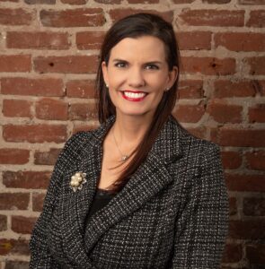 A photo of a woman with brown hair standing in front of a brick wall