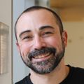 Michael Cohen, Ph.D. (OHSU) Michael Cohen, Ph.D., has buzzed dark and gray hair, dark facial hair, and a black shirt, smiling in the research building hallway.