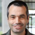 Adem Yildirim, Ph.D. has short black/gray hair and a gray jacket, smiling in the OHSU Knight Cancer building hallway.