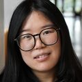 Li Xiang, Ph.D. has long black hair, a muted mauve jacket, eye glasses, and is standing in the hall of the OHSU Knight Cancer building.