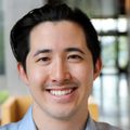 Michael Henderson has black hair combed back, a blue dress shirt, smiling in the hall of the Knight Cancer building at OHSU.