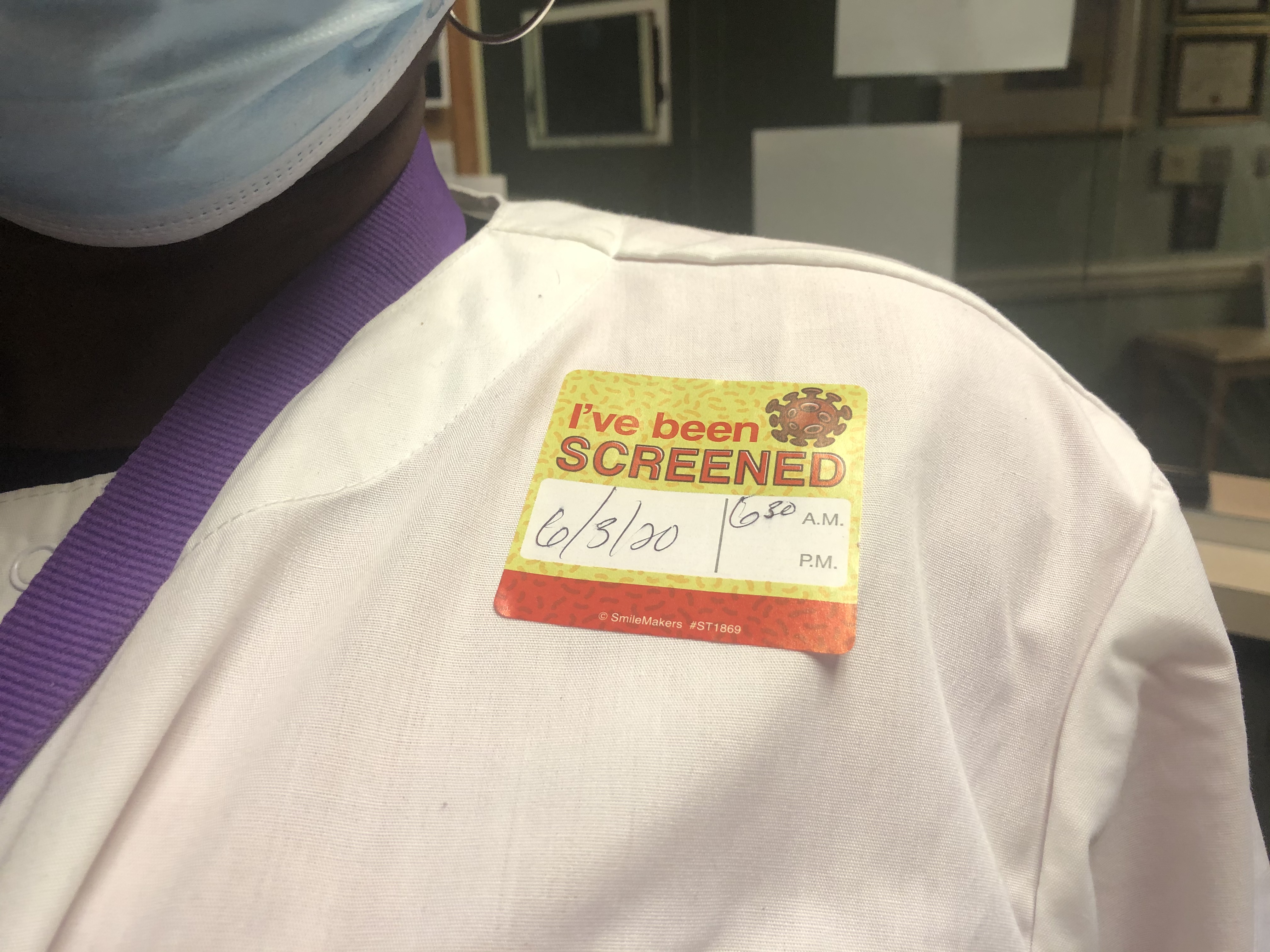 A team member wears an 'I've been screened' sticker. A team member wears an 'I've been screened' sticker.