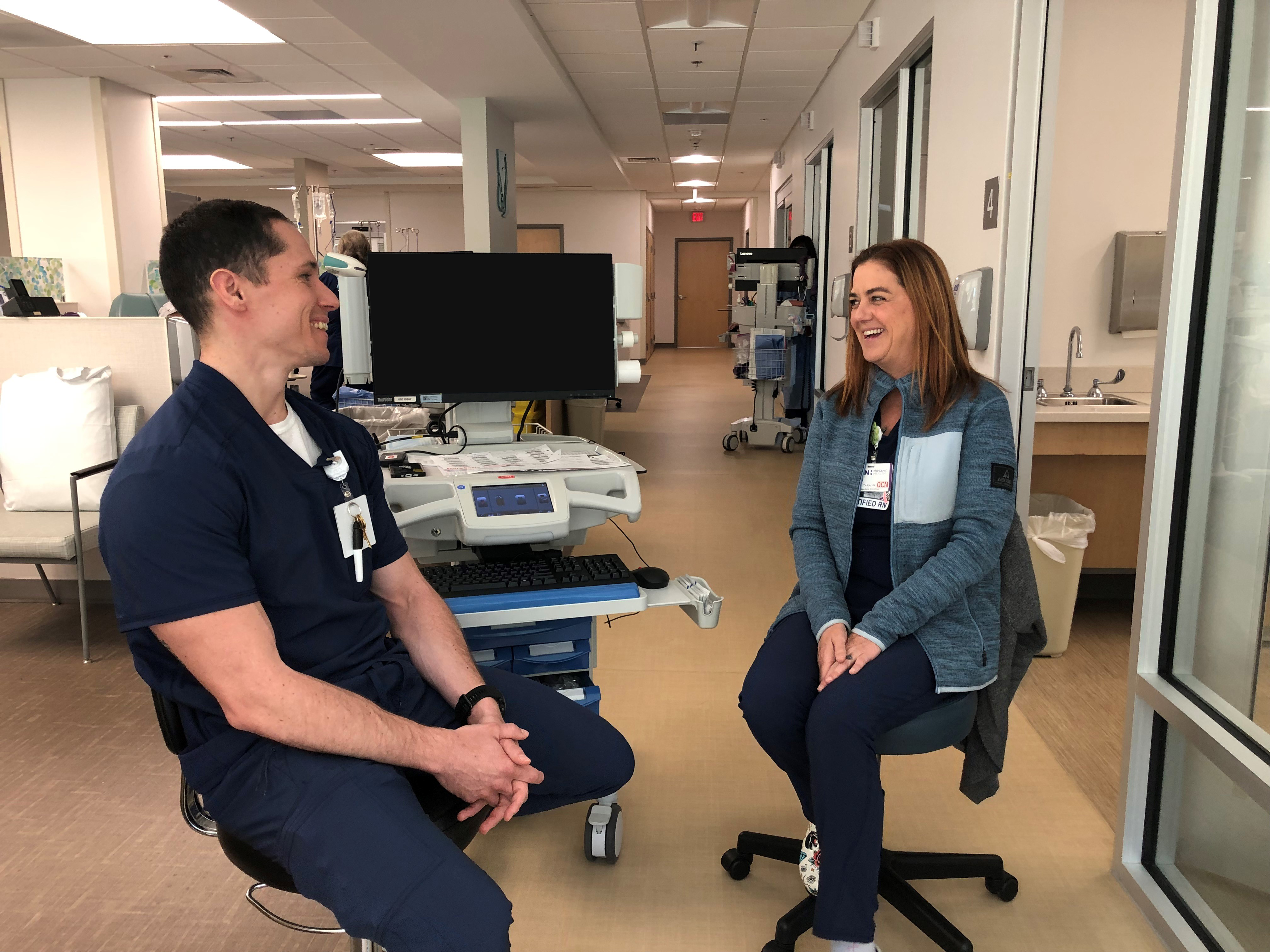Nurse Tara Wiggins and nurse Clint Hobbs sit and talk while dressed in scrubs.