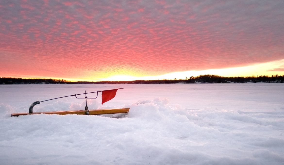 Wood ice fishing tip up on frozen lake with red flag