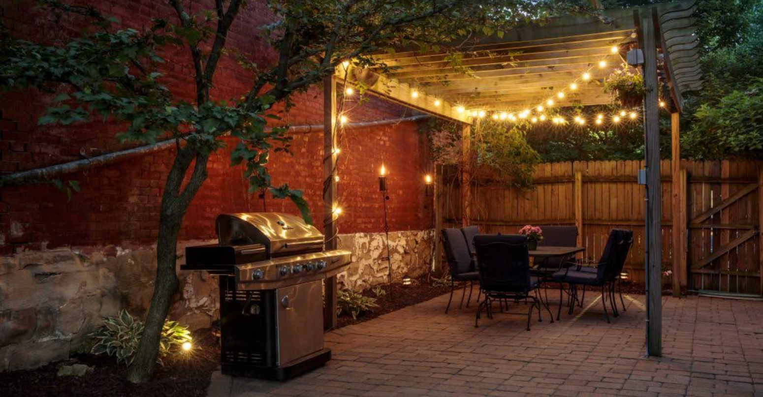 Bistro-style Edison string lights illuminating a backyard patio at dusk.