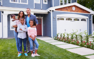 A family of four stands in front of a large two-story home in St. Louis, smiling — representing the move-up homeownership journey during National Homeownership Month.