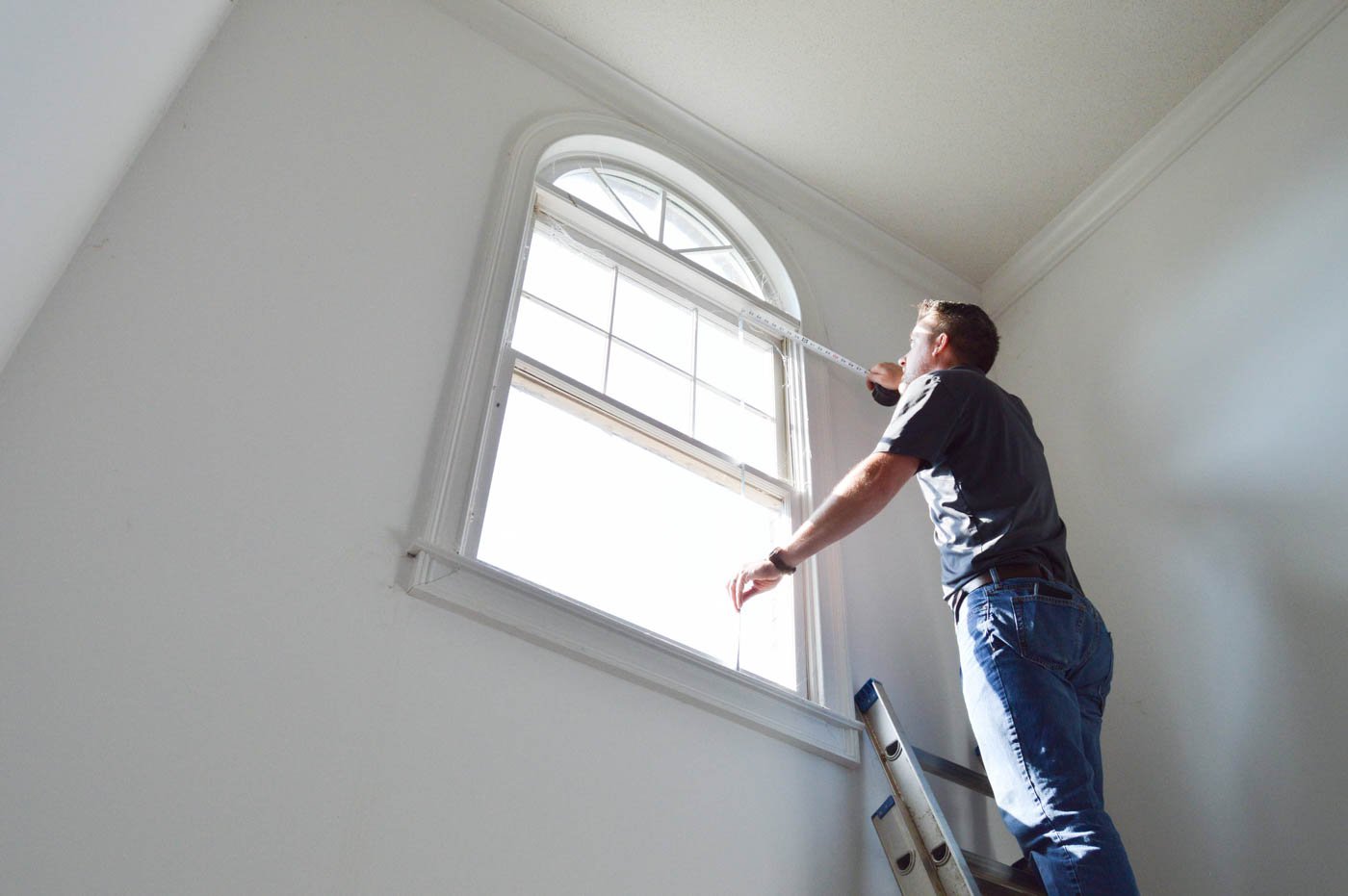 Man on ladder measuring windows