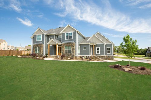 Large home with blue siding and stone details with green grass surrounding