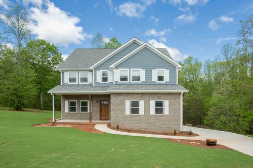 Exterior of blue and brick custom home with green grass and woods behind