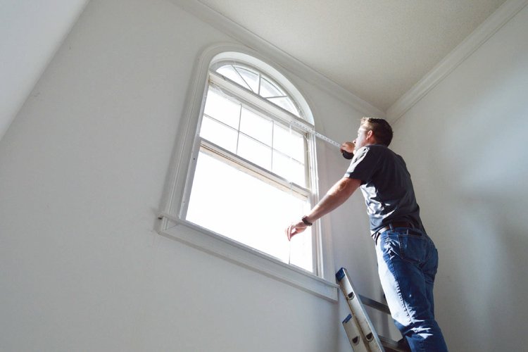 Man on a ladder measuring window