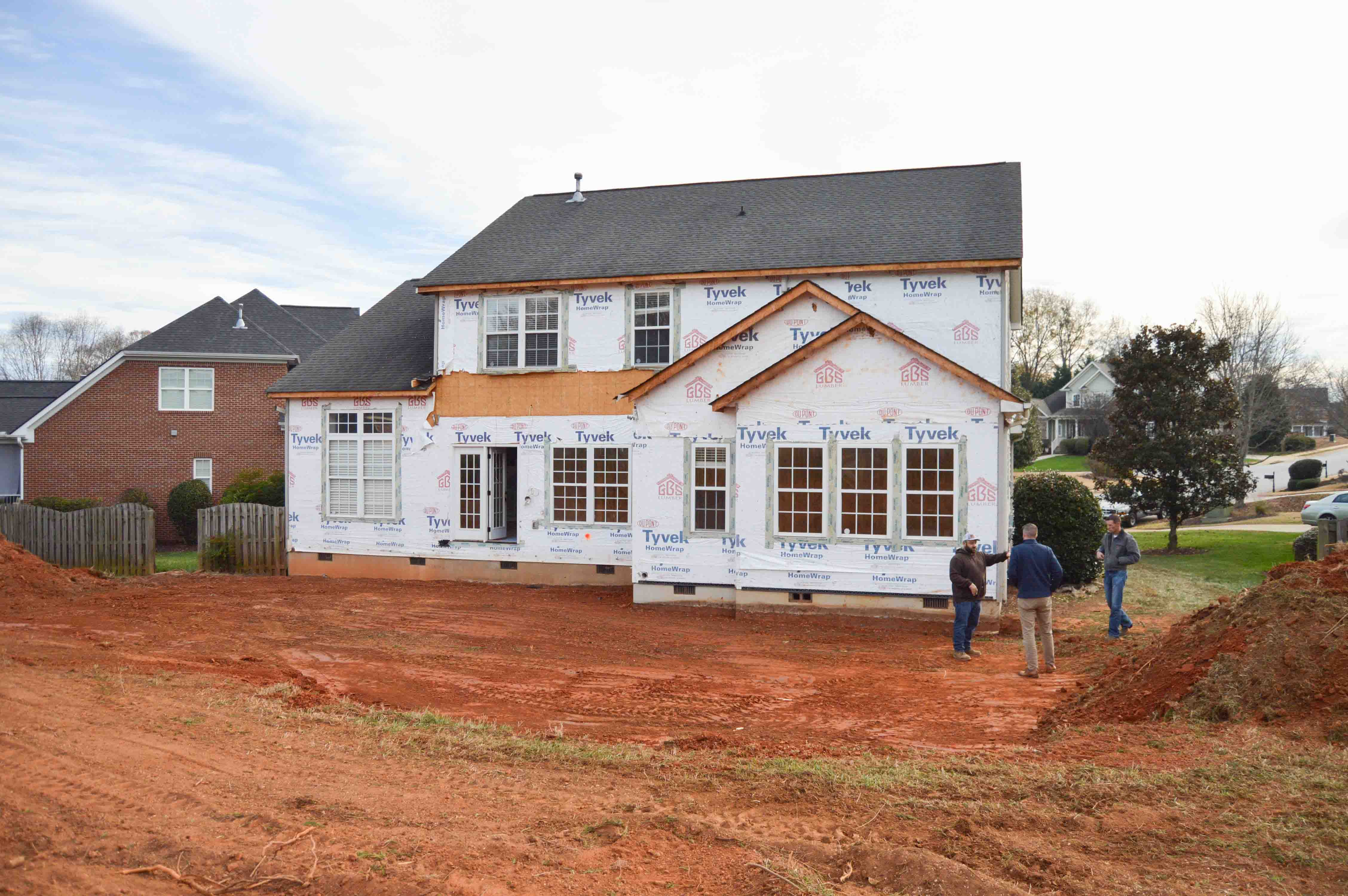 Partially built home with white house wrap and red dirt