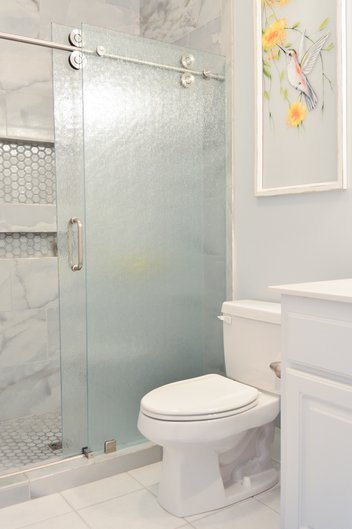 bathroom with toilet and gray tiled shower with glass door