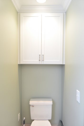 Green bathroom with white cabinet built in above toilet
