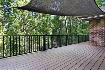 Brown deck on brick house with black railings and a shade sail