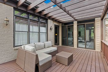 Custom deck with stained cedar pergola off of brown house with sunroom