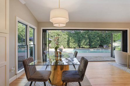 glass dining room table and chairs with accordion door open to backyard patio and pool
