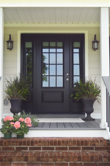 Front porch with black door and flowers on brick stairs
