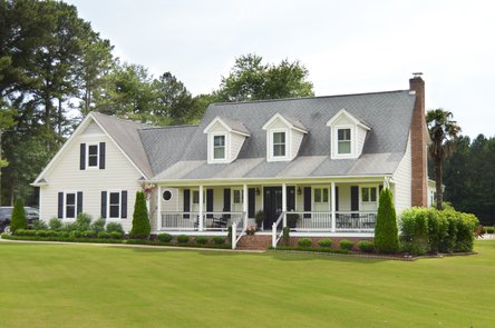 Beige house with white trim, black shutters, front porch, and green yard
