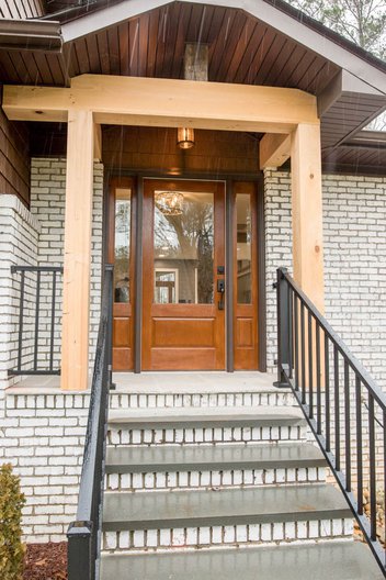 White brick home entryway with wooden beams and door