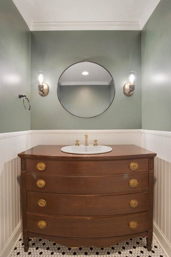 Green powder bathroom with gold sconces, wood vanity, and tiled floor