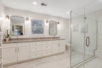 Neutral bathroom remodel with light grey walls, granite countertops, double vanity, and tiled glass shower