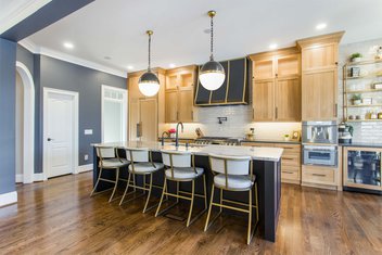 Kitchen with stained oak cabinets, navy blue walls, bold black fixtures, neutral backsplash and wood floors