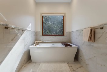 Freestanding tub centered in front of window in white marbled bathroom