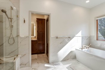 Bathroom with white marbled walls, shower and tub looking through door into sink area
