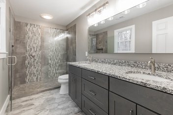 Bathroom with white and brown granite countertops, shaker cabinets hexagon flooring, diamond shower floor, glass accent mosaic band, 12x24 porcelain tile and satin nickel finishes
