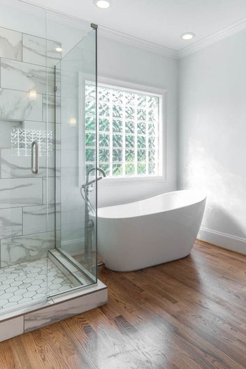 White bathroom with tiled shower, freestanding tub, glass block window and wood floors