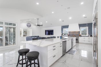 Large white kitchen with blue backsplash looking into living space with couch and TV