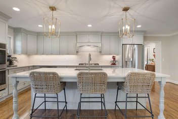 Kitchen with seafoam cabinet island, woven bar & counter Stools, and gold pendant lights