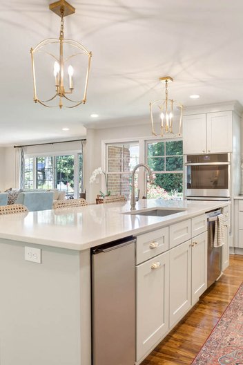 Kitchen with gold Chandelier pendant lights, white Torano Quartz countertop, and seafoam cabinet island