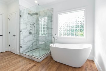 White bathroom with tiled shower, freestanding tub, glass block window and wood floors
