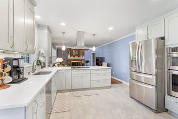 Aleutian blue kitchen with white countertops looking into living room with brick fireplace