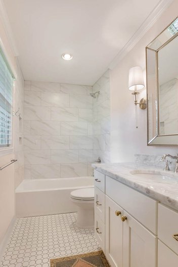 White bathroom with tiled shower and floor, wall sconce, and Polished Torano Quartz countertop