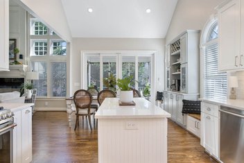White kitchen with island looking into dining area with lots of windows and natural light