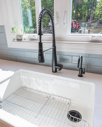 White sink with blue subway tile and black faucet fixtures by a window looking into yard