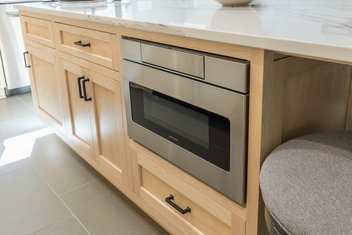 microwave under the counter built into white oak cabinets with white countertop