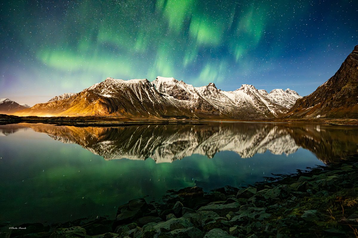 Northern lights over snow-capped peaks reflected in a still fjord in Lofoten, Norway