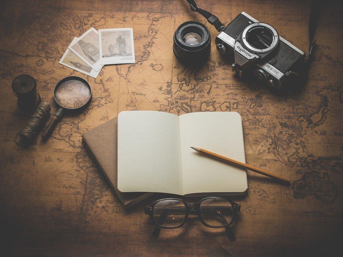 Camera, lenses, a map, photographs and an open notebook arranged on a tabletop