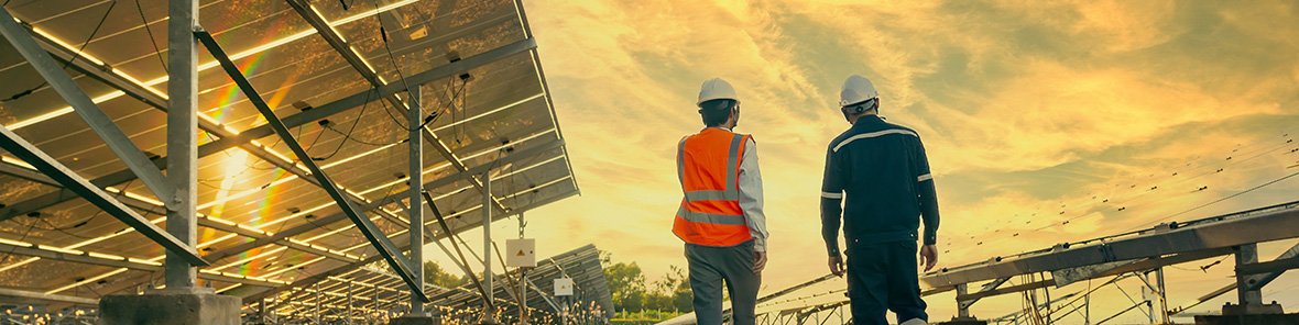 Two workers walking along a series of panels in a field, low perspective, sunrise or sunset